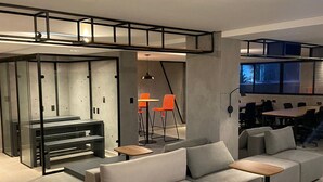 Un salon moderne avec un canapé d’angle, un ascenseur en verre et un coin repas doté de chaises orange.