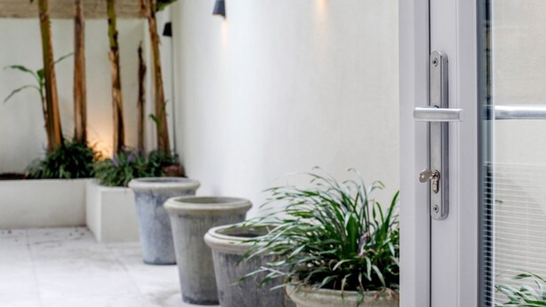Un espacio exterior moderno con pared blanca, plantas en macetas y puerta de vidrio.