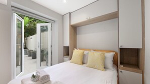 Una habitación de hotel moderna con una cama grande, un cabecero de madera y un ventanal corredero que da a un espacio exterior con plantas en macetas.