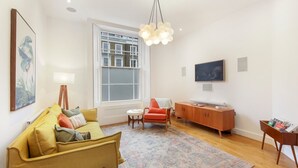 Una sala moderna con un sofá, un sillón rojo, un mueble de madera y un televisor en la pared.
