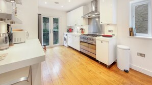 Una cocina moderna con armarios blancos, una campana extractora de acero inoxidable, horno empotrado y lavadora.