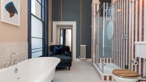 A modern bathroom with a freestanding bathtub, a shower enclosure, and a toilet with a wooden seat.