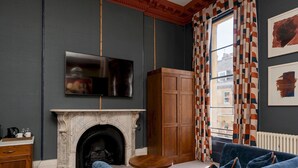 A room with a fireplace, a television mounted on the wall, a wooden cabinet, a blue sofa, and patterned curtains.