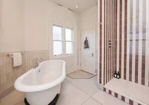 Un baño con una bañera independiente, zona de ducha con puerta de cristal y suelo de baldosas.