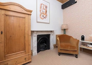 Una habitación con un armario de madera, chimenea, sofá y un papel tapiz estampado.
