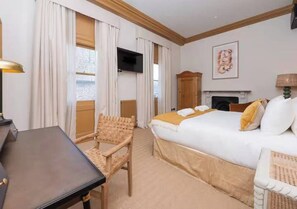 A hotel room with a bed, a desk, a chair, a television, and a fireplace.
