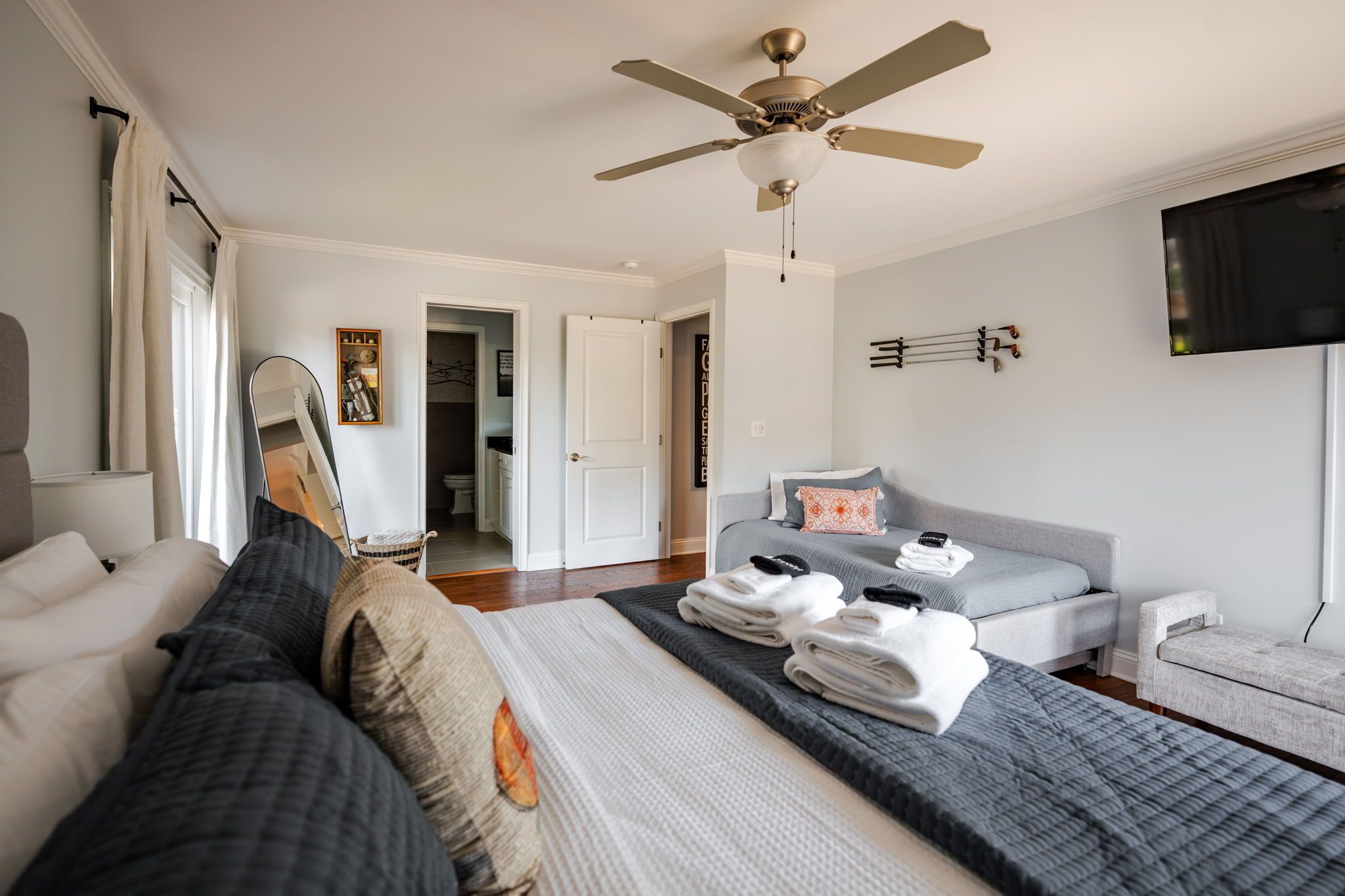 Ein modernes Schlafzimmer mit Bett, einer Couch, einem Deckenventilator, einem Fernseher und einer Tür zu einem anderen Raum.