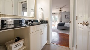 Une salle de bain moderne avec un grand miroir, des meubles blancs et un panier sur lequel est écrit : « Vous avez oublié quelque chose ? »