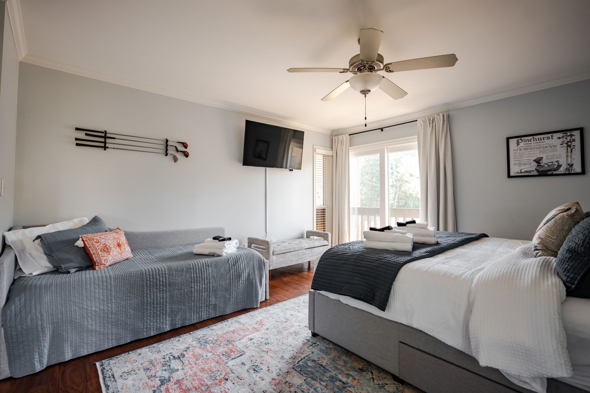 A bedroom with two beds, a ceiling fan, a TV, and a window with curtains.