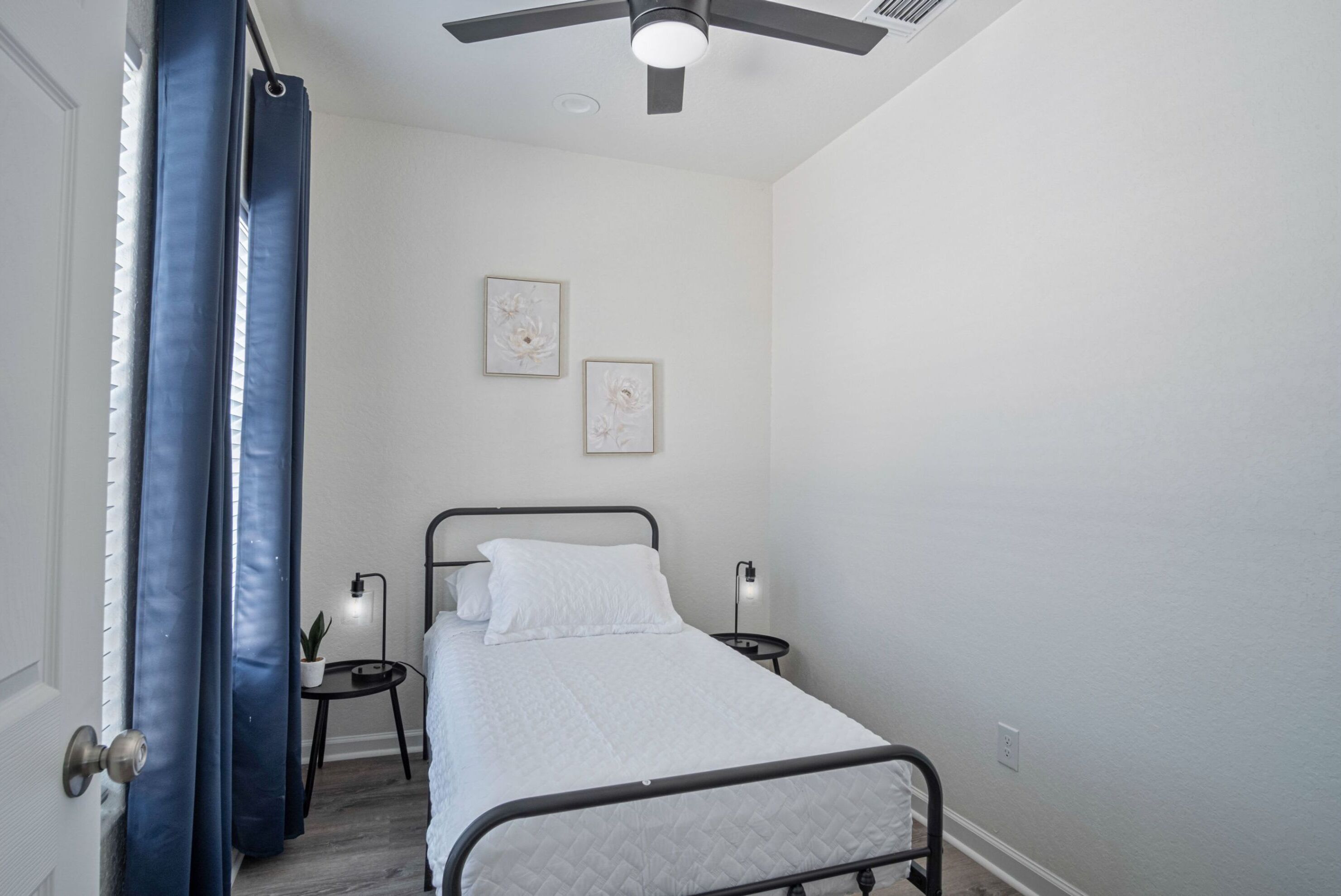 A bedroom with a bed, two bedside tables, a ceiling fan, and two wall-mounted picture frames.