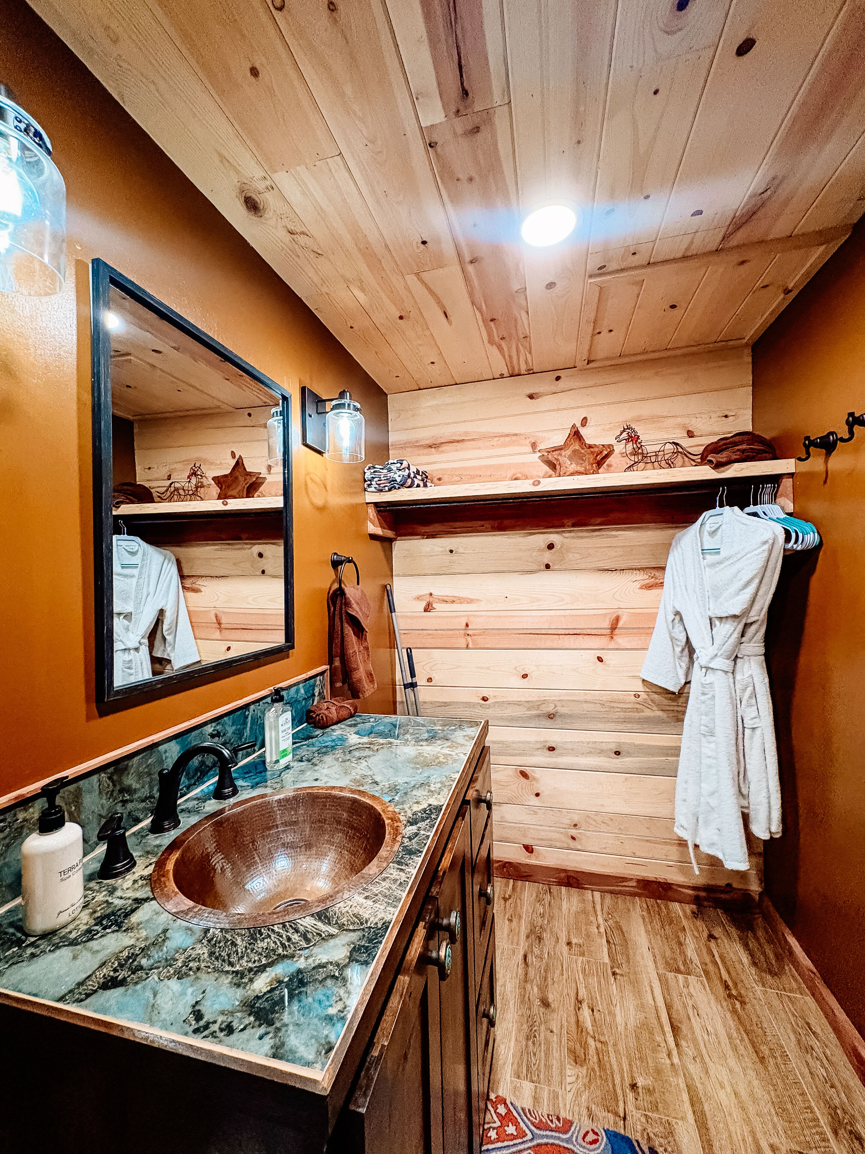 Un baño de cabaña de madera con un lavabo de madera, un espejo, un perchero y una bata colgada en la pared.