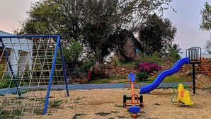 Un parque infantil con un tobogán azul, una red de escalada y un arenero con diversos juegos.