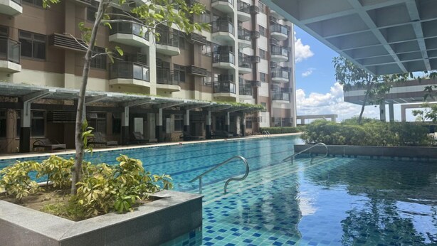 A swimming pool area with a view of a multi-story building, including balconies and a covered walkway. - Levi & Moon Relax and Chill (Pasay City)