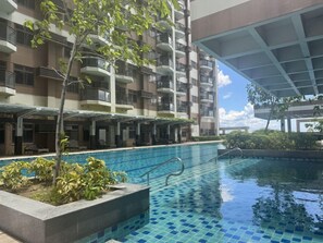 Ein Poolbereich mit Blick auf ein mehrstöckiges Gebäude, inklusive Balkone und einem überdachten Gang.