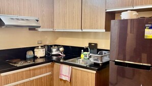 A modern kitchen with wooden cabinets, a black countertop, a stainless steel sink, and a refrigerator. - Levi & Moon Relax and Chill (Pasay City)