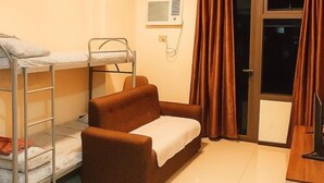 A small, well-lit room with a bunk bed, a brown sofa, a desk, and a window with curtains. - Levi & Moon Relax and Chill (Pasay City)