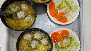 Una bandeja con cuencos de sopa, platos de verduras cortadas y un tazón pequeño de vegetales encurtidos rojos.