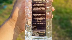 Una botella de plástico transparente con agua potable, mostrando una etiqueta con un diseño de árbol y montaña, sostenida por una mano.