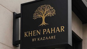 Un letrero negro con letras doradas para Khen Pahar by Kazaare, que presenta un logo con un árbol.