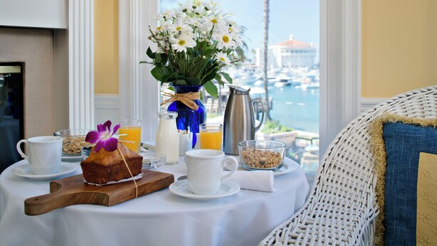 A breakfast table with a vase of flowers, a coffee pot, and a view of the marina. - Snug Harbor Inn (Avalon)