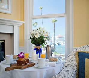 A breakfast table with a vase of flowers, a coffee pot, and a view of the marina. - Snug Harbor Inn (Avalon)
