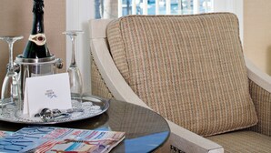 A room with a view of palm trees and a balcony. There is a chair, a table with a bottle of champagne, glasses, and a magazine. - Snug Harbor Inn (Avalon)