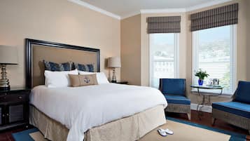 A hotel room with a large bed, two chairs, a small table, and a window with blinds.