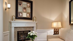 A living room with a fireplace, a coffee table with a book, a lamp, and a couch. - Snug Harbor Inn (Avalon)