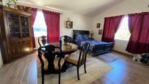 Um quarto com uma cama, uma mesa de jantar com cadeiras, um armário de madeira e uma janela com cortinas vermelhas.