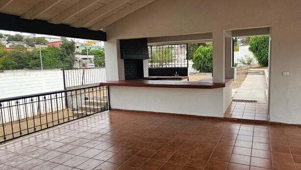 Uma área de pátio ao ar livre com piso ladrilhado, uma churrasqueira preta e vista para a rua.