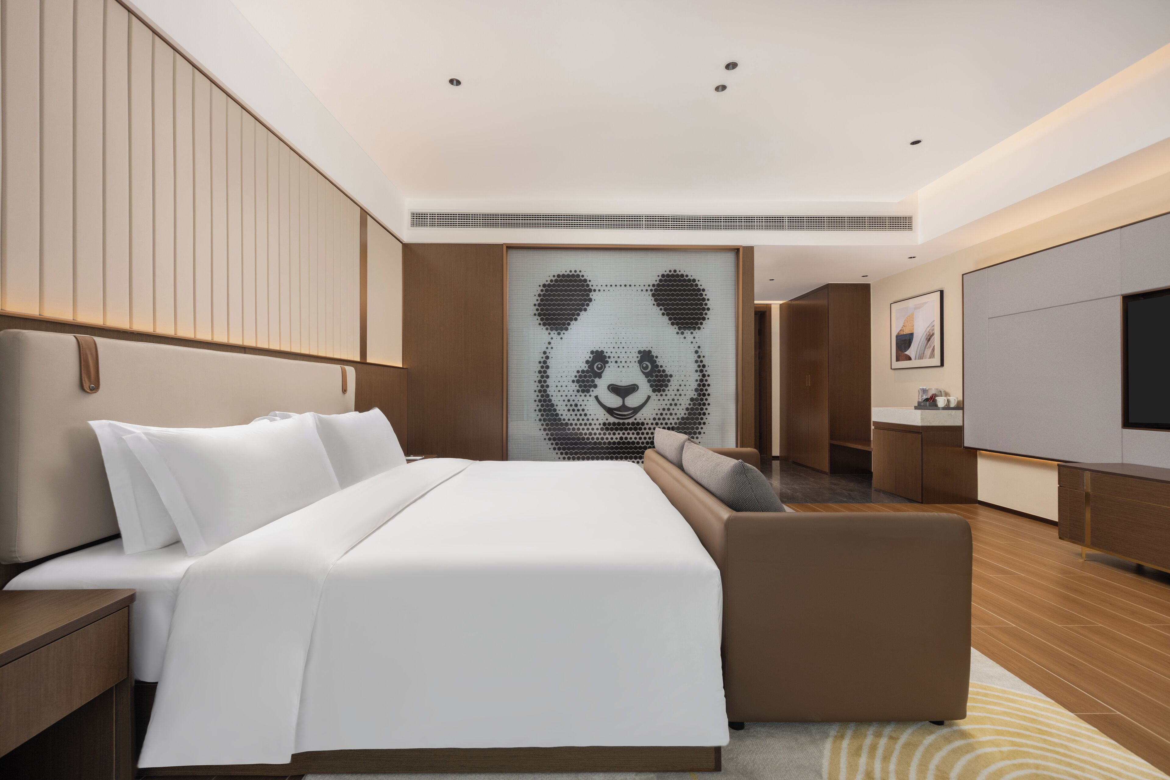 A modern hotel room with a large bed, a sofa, a TV, and a panda-themed artwork on the wall.