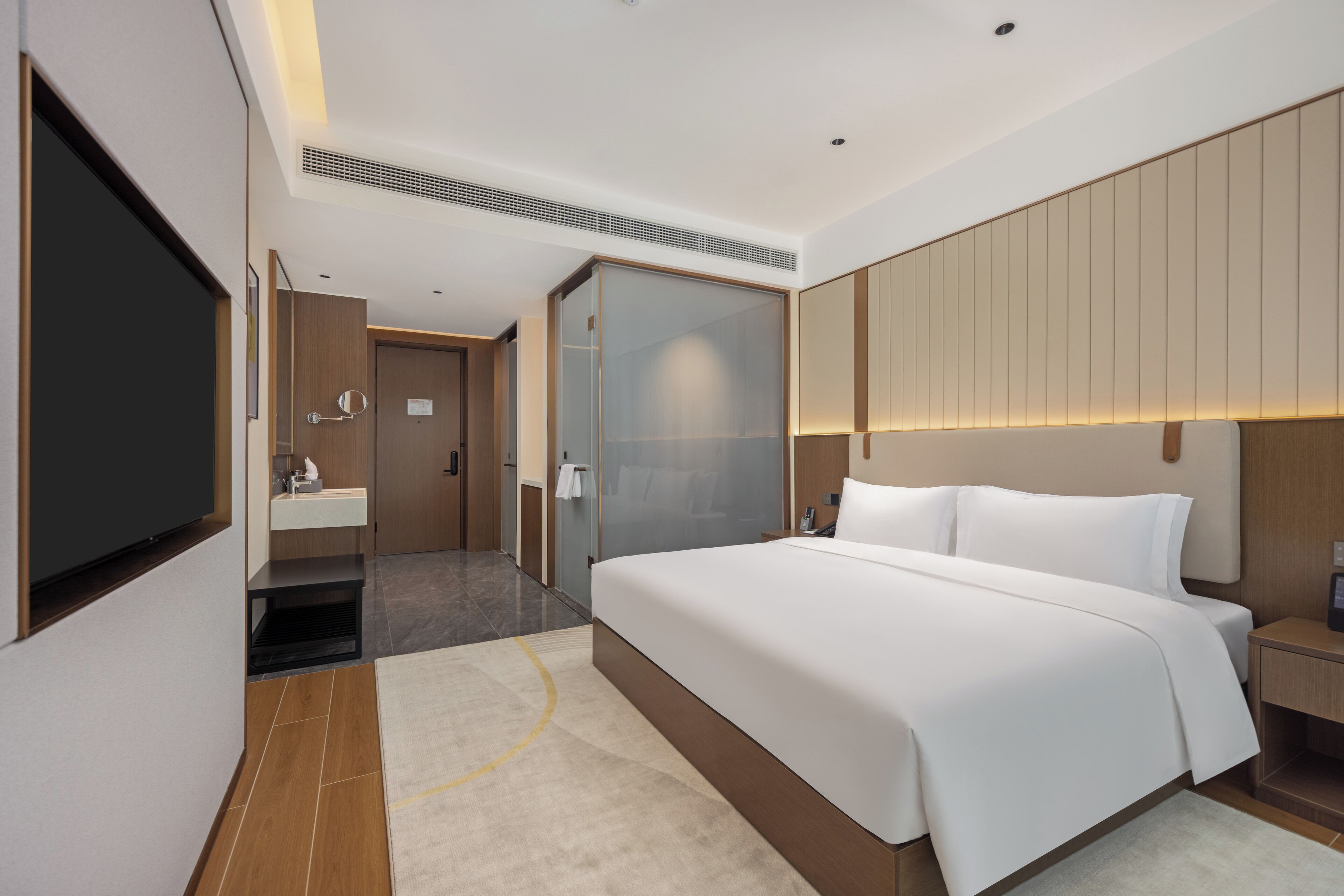 A modern hotel room with a large bed, a flat-screen TV, a bathroom with a mirror and sink, and a sliding door closet.