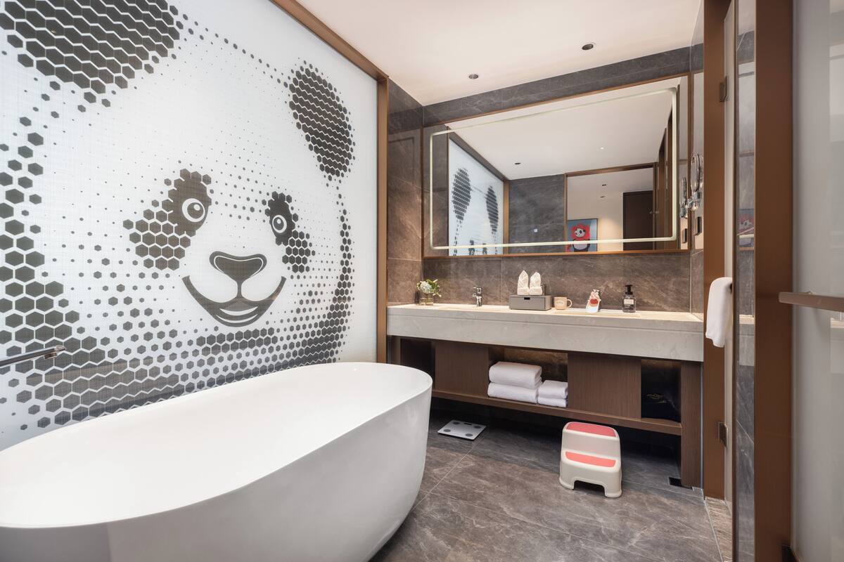 Ein modernes Badezimmer mit einem großen Spiegel, einer freistehenden Badewanne und Wandkunst aus Mosaik.