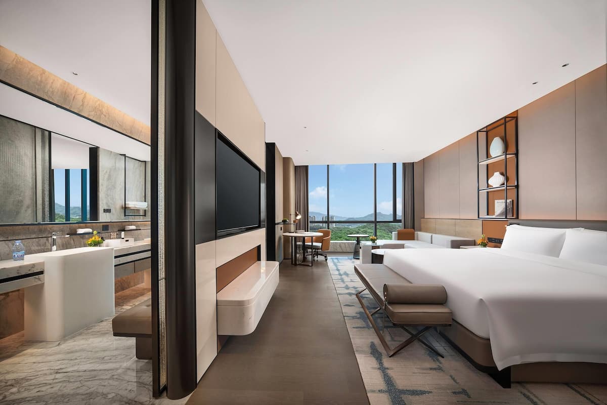 Een moderne hotelkamer met een groot bed, een televisie, een bureau en een badkamer met een grote spiegel.