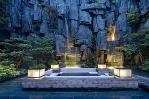 A rock garden with a waterfall, seating area, and illuminated planters.