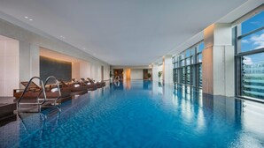 An indoor swimming pool with clear blue water, lounge chairs, and a view of the city through large windows. - Wyndham Grand Shenzhen Guangming (Shenzhen)