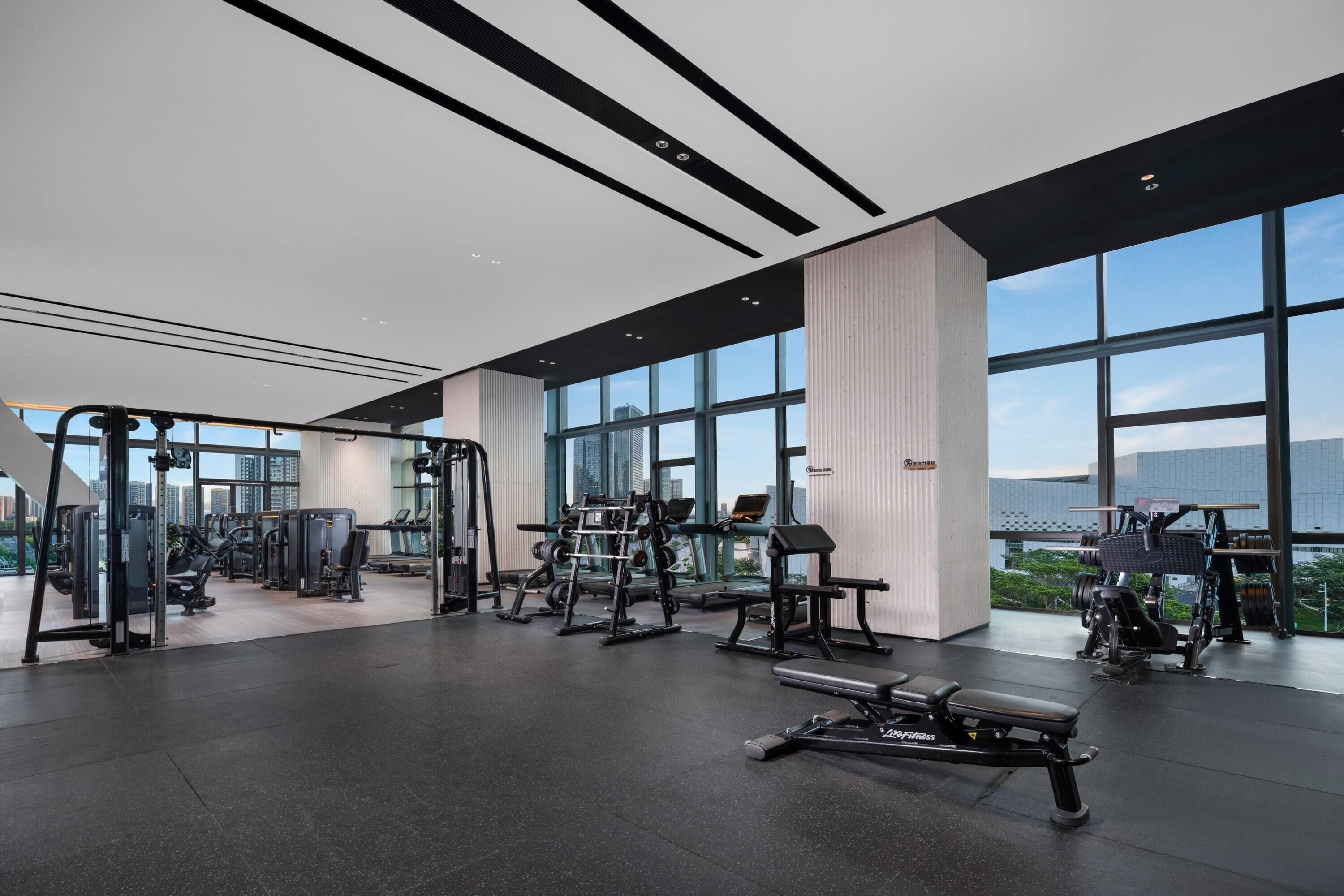 Een moderne sportschool met diverse trainingsapparaten, grote ramen en een uitzicht op de stadsgezicht.