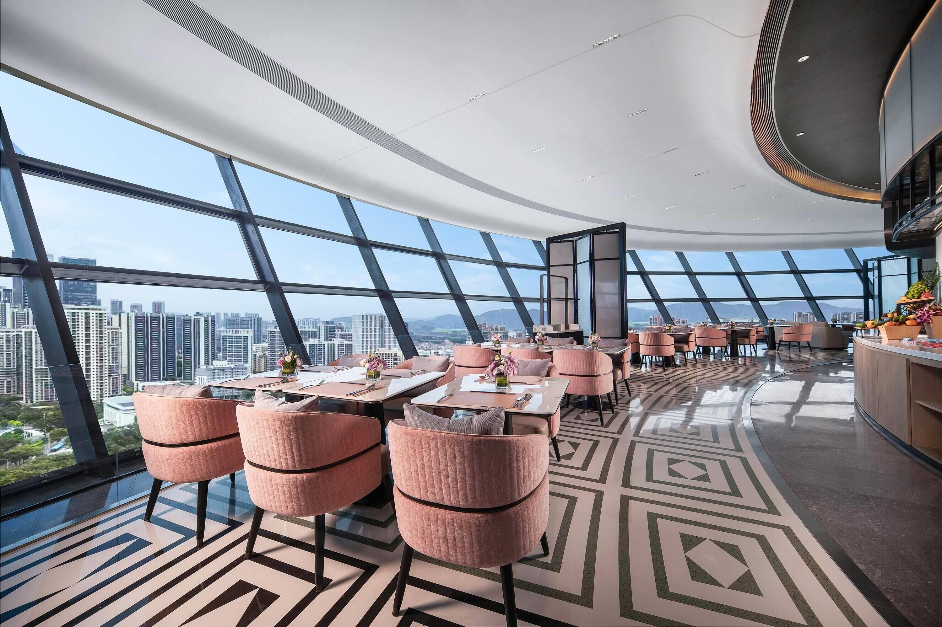 Un restaurante moderno con vistas panorámicas a la ciudad, que presenta un suelo con estampado geométrico y sillas tapizadas en rosa.