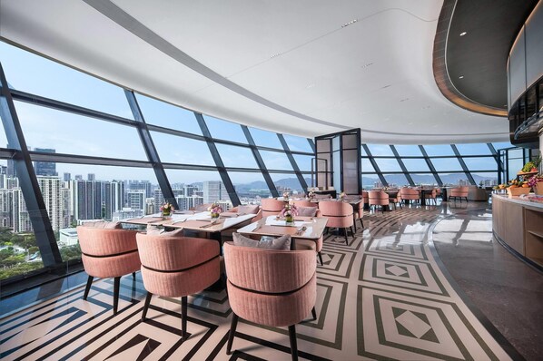 Un restaurante moderno con vistas panorámicas a la ciudad, que presenta un suelo con estampado geométrico y sillas tapizadas en rosa.