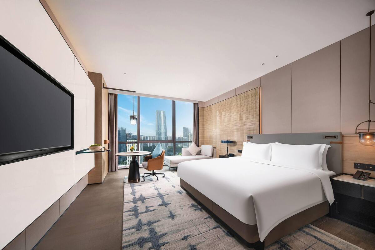 Een moderne hotelkamer met een groot bed, een bureau, een stoel, een televisie en uitzicht over de stad.