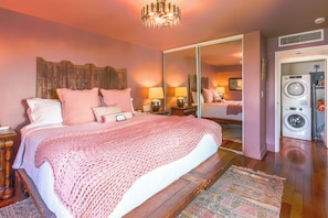 A bedroom with a large bed, a mirror, a washing machine, and a chandelier. - Tropical Lotus- Cozy 3 bedroom, 3 bath with an ocean view, pool, gym, & tennis (St Thomas)