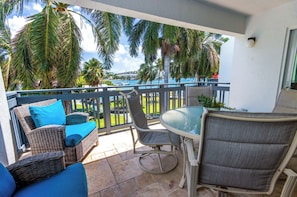 A balcony with wicker furniture, a glass table, and a view of a marina. - Tropical Lotus- Cozy 3 bedroom, 3 bath with an ocean view, pool, gym, & tennis (St Thomas)