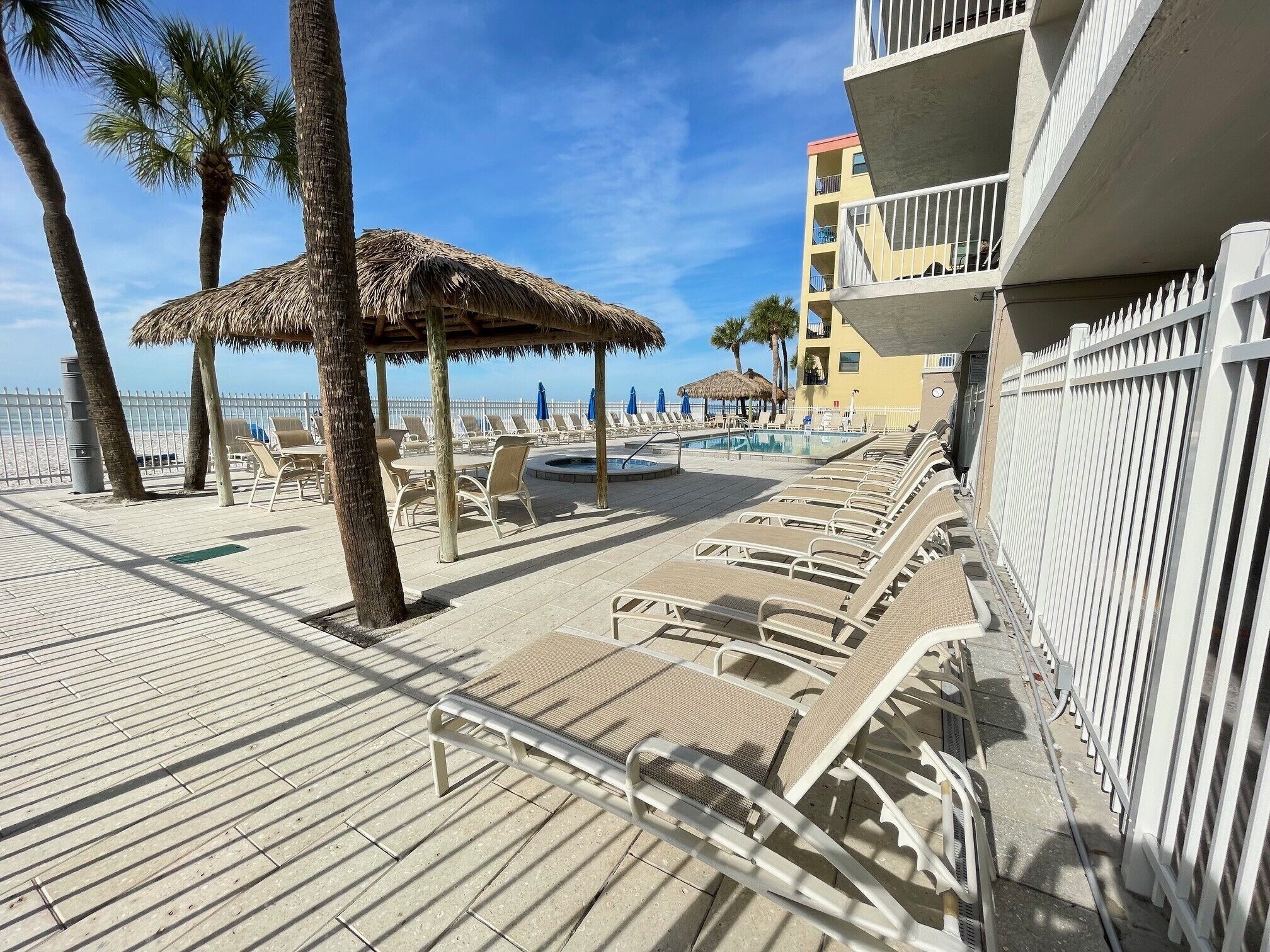 A beachside hotel with a pool, lounge chairs, and a thatched umbrella.