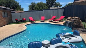 A swimming pool with inflatable rings, red lounge chairs, and a waterfall feature. - Ultimate Game Day Stay, 3BR House +Pool Near AT&T Stadium but far from the noise (Arlington)