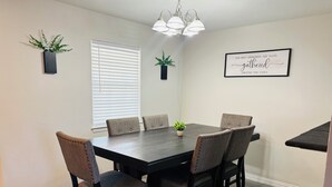 A dining room with a dark wooden table, six upholstered chairs, a chandelier, and two potted plants. - Ultimate Game Day Stay, 3BR House +Pool Near AT&T Stadium but far from the noise (Arlington)
