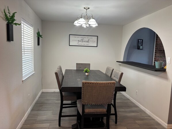 A dining area with a dark wooden table, six upholstered chairs, a potted plant, a chandelier, and a framed quote on the wall. - Ultimate Game Day Stay, 3BR House +Pool Near AT&T Stadium but far from the noise (Arlington)