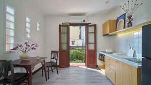 A kitchen with a dining area, wooden cabinets, a white tiled backsplash, and a view through an open door to a balcony. - Express by M Village Cach Mang Thang 8, a brand of Modern Village Lifestyle (Ho Chi Minh City)
