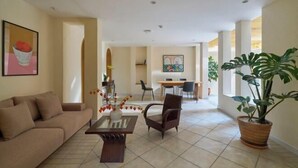 A living room with a sofa, a coffee table, and a dining area with chairs and a table. There is a large potted plant and a painting on the wall. - Express by M Village Cach Mang Thang 8, a brand of Modern Village Lifestyle (Ho Chi Minh City)