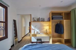 A bedroom with a bed, a desk with a lamp, a wardrobe, and a mirror.