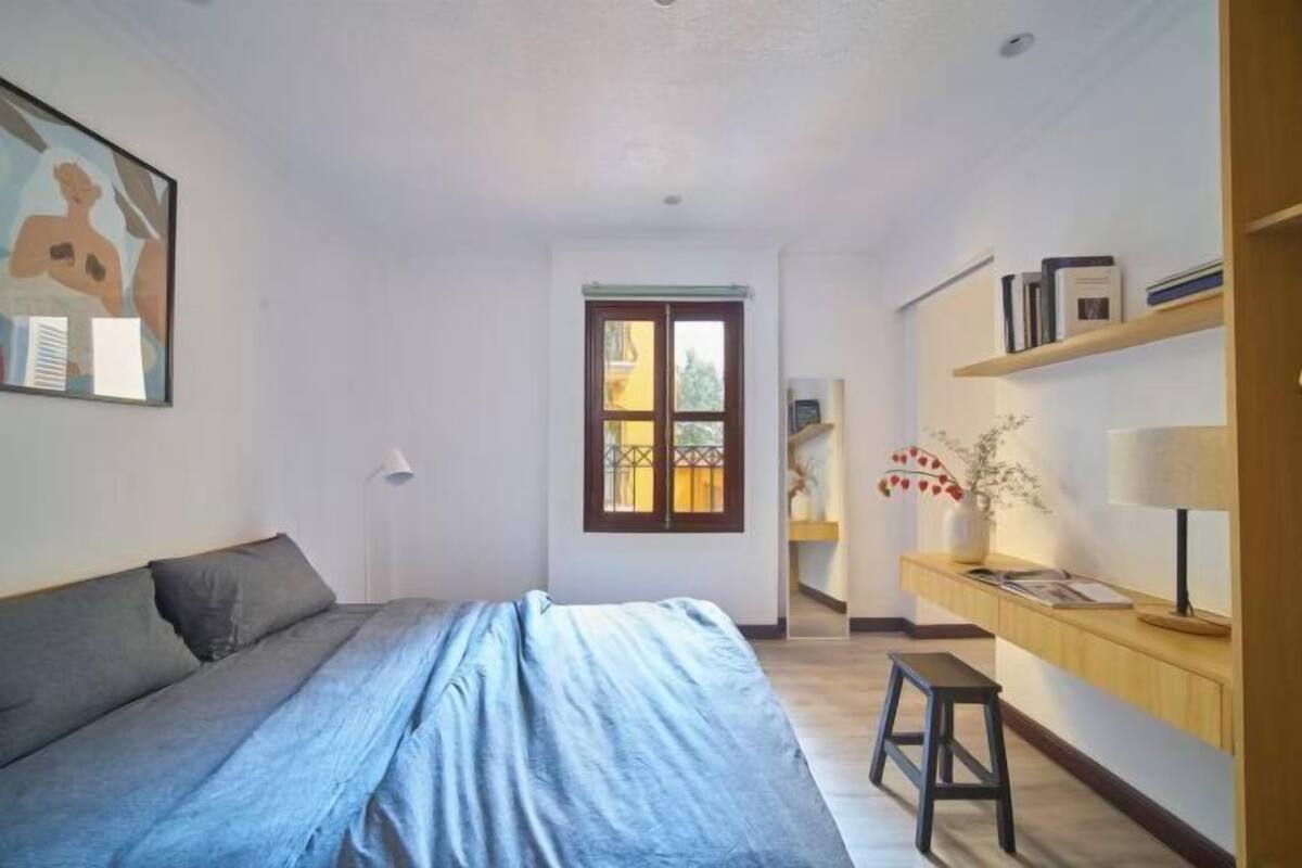 Ein Schlafzimmer mit Bett, Nachttisch, Fenster und Bücherregal.